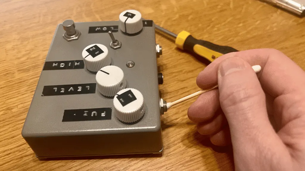 Close-up of cleaning a pedal jack socket from the outside, where dark residue signals oxidation.