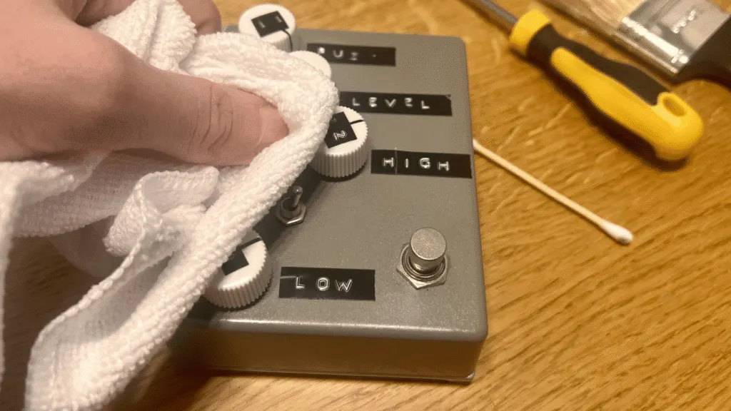 Close-up of a dry microfibre cloth being used to clean the enclosure of a guitar pedal.
