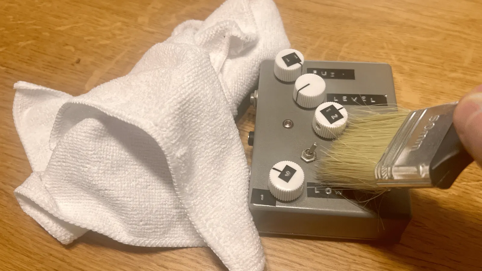 Close-up of a soft paintbrush being used to dust a guitar pedal during cleaning.