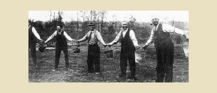 Historical black and white photo of firefighters passing water buckets in chain formation