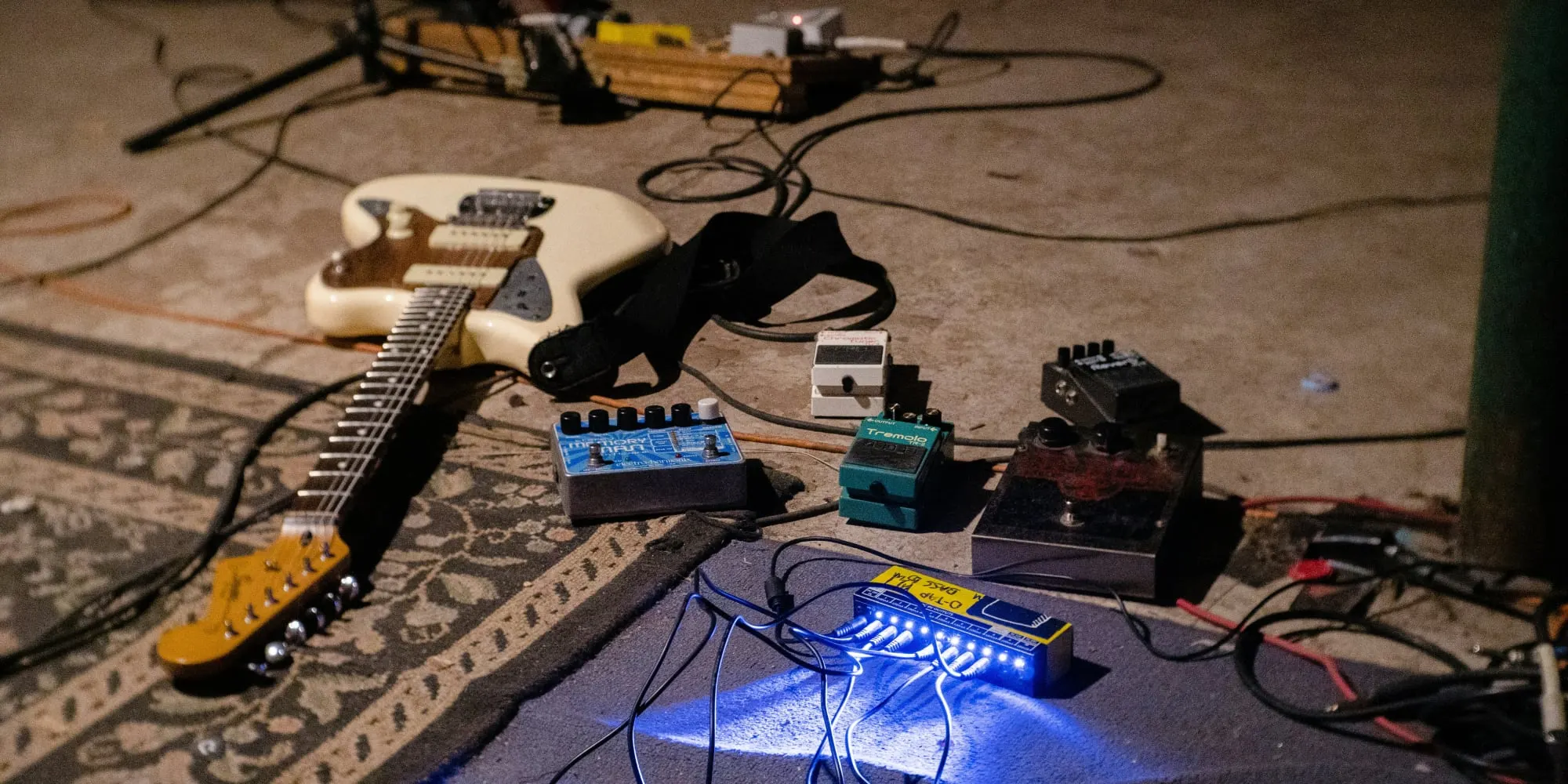 White electric guitar leaning on the floor next to a few guitar pedals