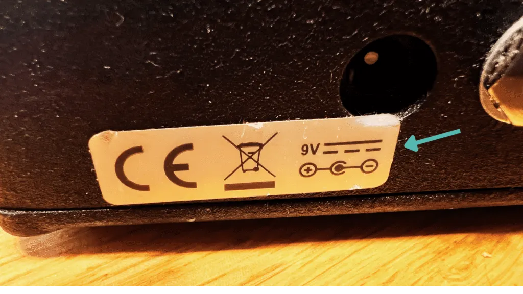 Close-up of a guitar pedal power sticker, showing the voltage and polarity specs to match your supply.