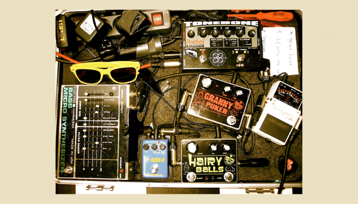 Cluttered guitar pedalboard with tangled cables and various colorful effects pedals.